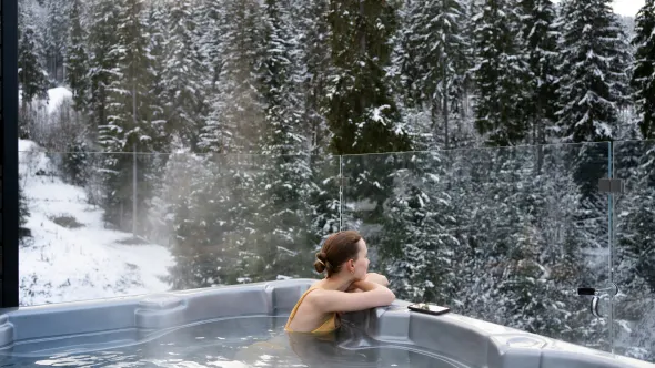 Eine Frau sitzt in einem Whirlpool in verschneiter Winterlandschaft.