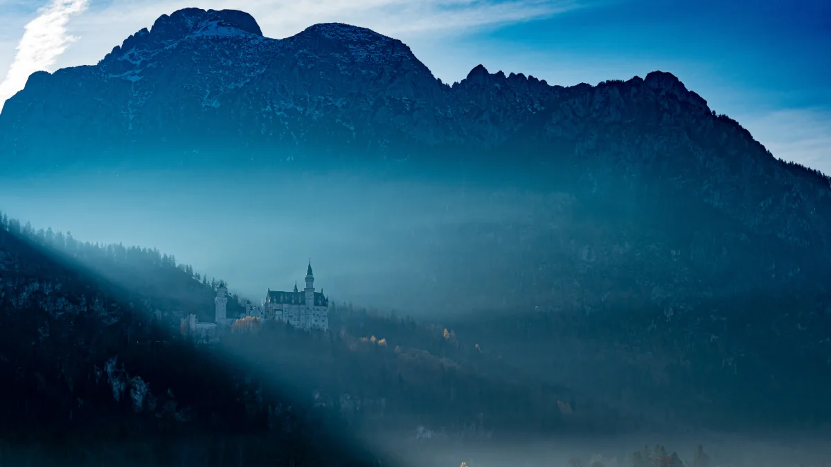 Neuschwanstein Slot i skumringen, beliggende mellem Alpernes tågede bjergtoppe.