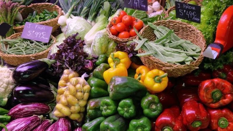 Aubergines (eggplant), bellpeppers and beans at green grocer's stand at local market hall 