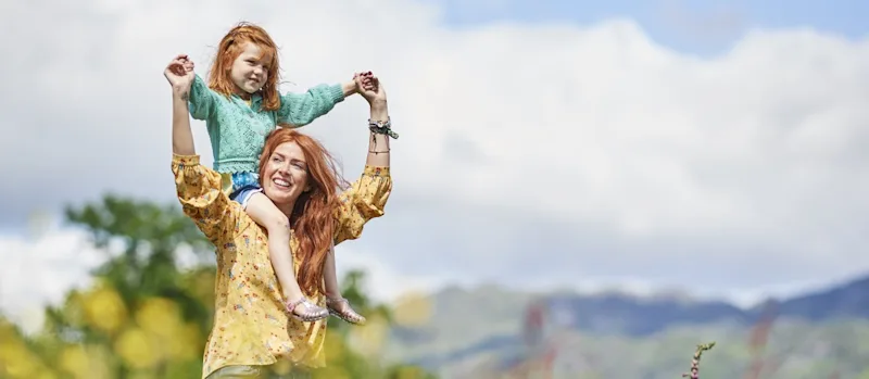 Mother walking through a meadow with child on her shoulders at Loch Lomond Holiday Park in Argyll, Scotland