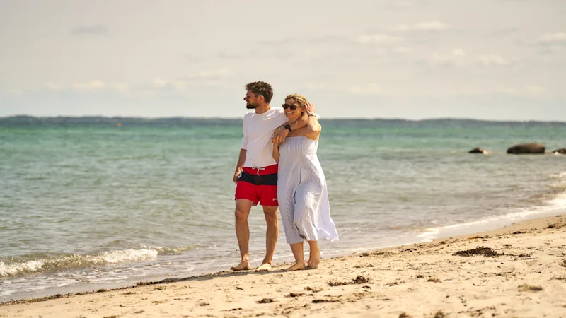 Ein Mann und eine Frau gehen Arm in Arm am Strand spazieren.