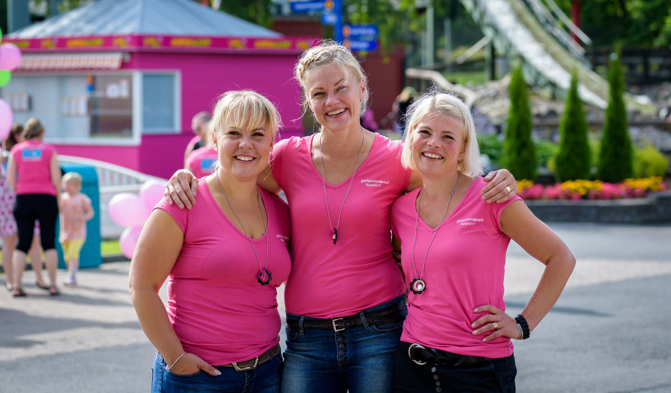 Kolme naista hymyilee pinkit puserot päällä Särkänniemessä.