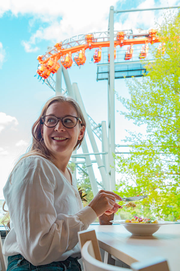 Nainen ruokailee Särkänniemen ravintola Ilossa, ja taustalla näkyy Tornado-huvilaite.