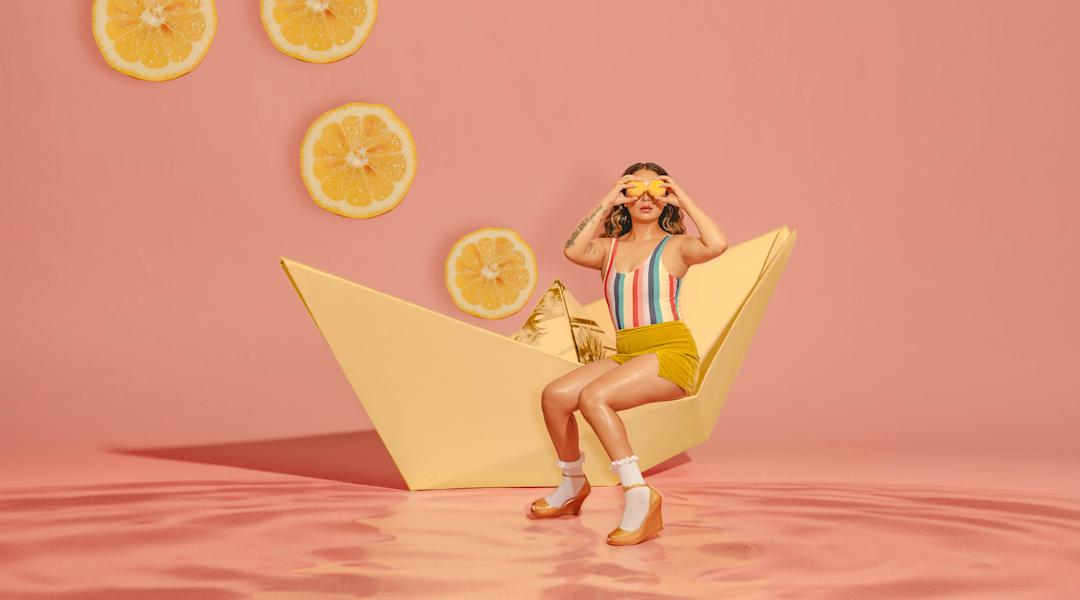 A woman in a paper boat holding lemons up to her eyes