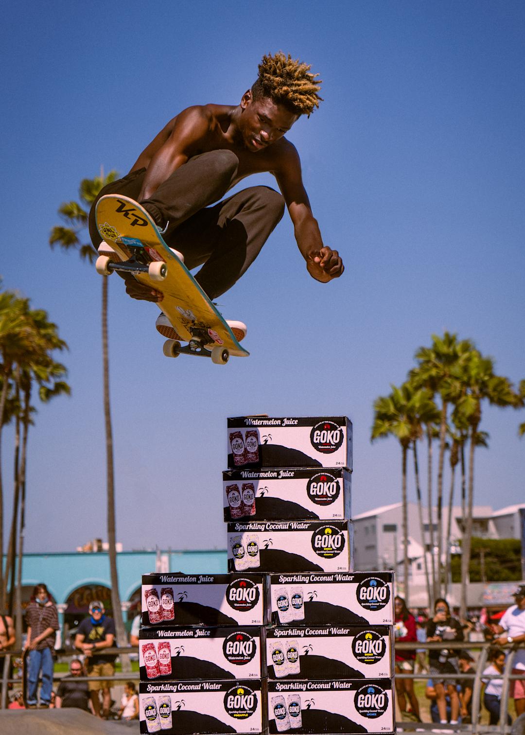 A man on a skateboard jumping over several cases of Goko.