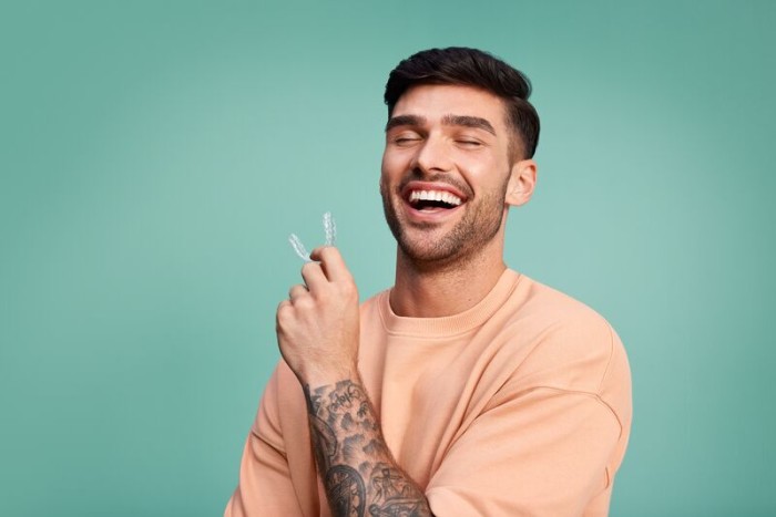 Hombre sosteniendo un alineador invisible de DR SMILE para su tratamiento de alineación dental de una mordida abierta con ortodoncia invisible