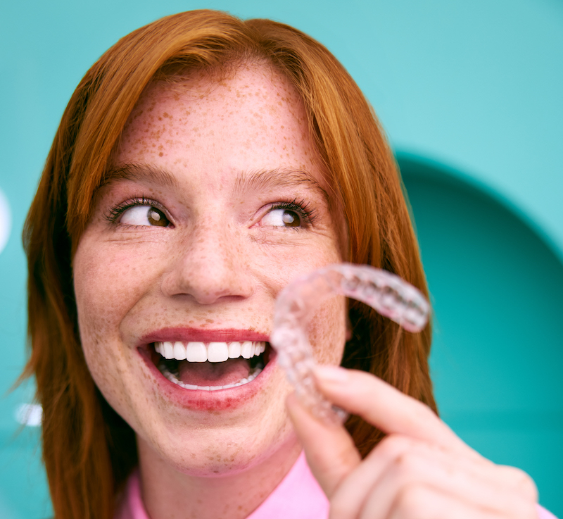 [CRO] Hero - Aligner - Smile - Look to the left - Side - Hand - Pink Shirt - Blue - Background - Desktop