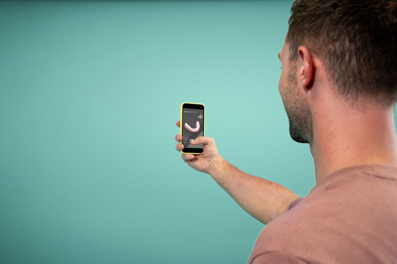 Mann, der sich einer Zahnausrichtungsbehandlung mit unsichtbaren DR SMILE-Alignern unterzieht, überprüft den Fortschritt über die App