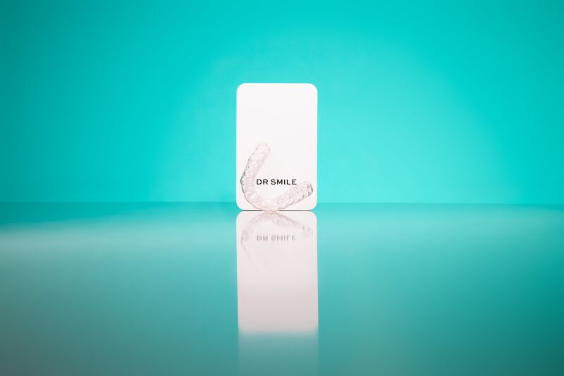 Alineadores y caja de DR SMILE sobre fondo azul verdoso