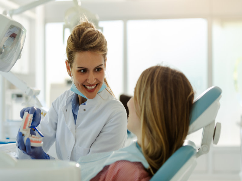 Schöne Zahnärztin zeigt der Patientin, wie sie ihre Zähne richtig putzen soll.