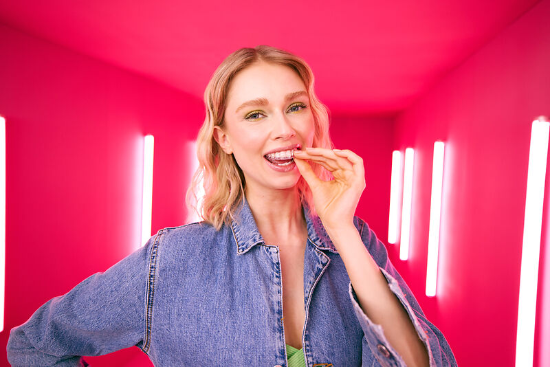 [CRO] Blond - Woman - Aligner - Hand in the teeth - Looking to camera - Pink - Light - Background - Desktop