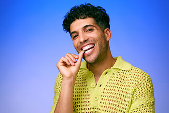 [CRO] Man - Brunette - Curly hair - Smile - Finger on mouth - Looking left - Green - Knitting - T-shirt - Blue - Gradient - Background - Mobile