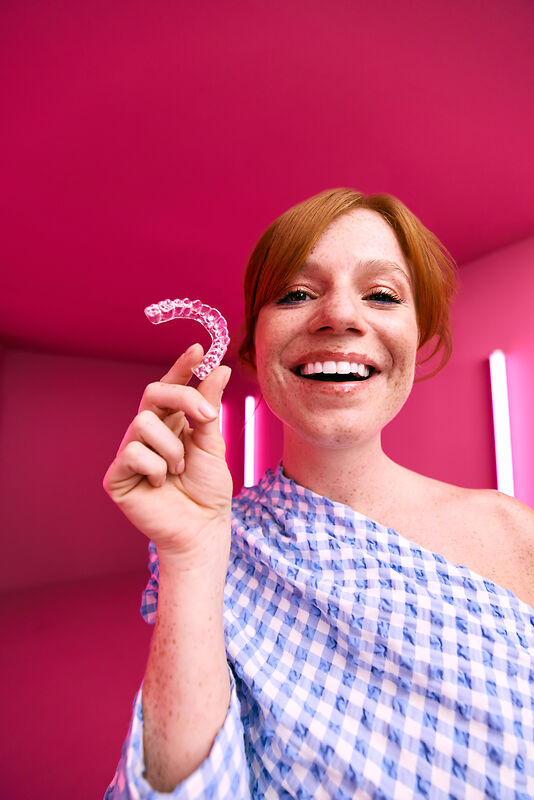 [CRO] Woman - Ginger - Checkered shirt - Freckles - Aligner in hand - Looking to camera - Pink - Light - Background - Desktop