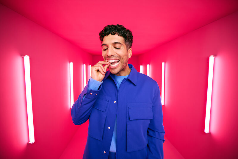 [CRO] Man - Brunette - Curly hair - Smile - Aligner - Looking down - Blue - Jacket - T-shirt - Pink - Light - Background - Desktop
