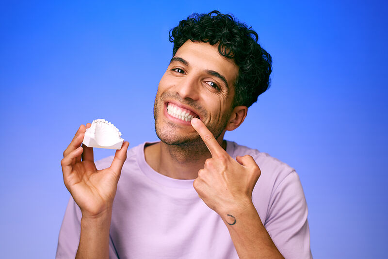 [CRO] Man - Brunette - Curly hair - Dental arch - Looking left - Finger on mouth - Smile - Lilac - T-shirt - Blue - Gradient - Background - Desktop