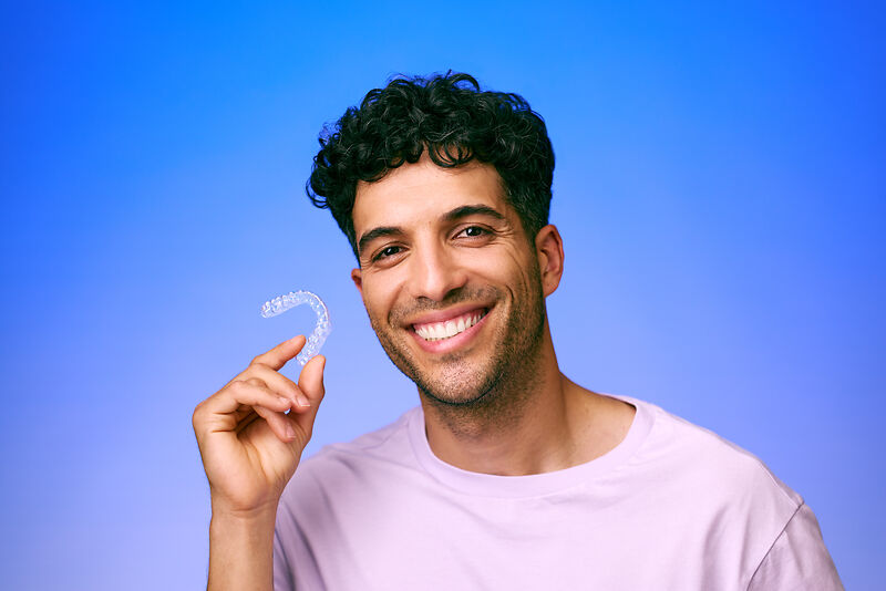 [CRO] Man - Brunette - Curly hair - Looking front - Aligner - Smile - Lilac - T-shirt - Blue - Gradient - Background - Desktop