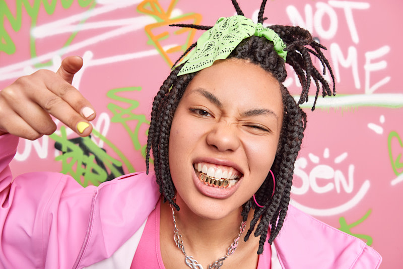 goldene Grillz auf den unteren Frontzähnen im Mund einer jungen Frau, Foto von wayhomestudio via Freepik