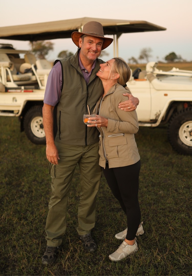 Couple Standing & Smiling with Drink in Hand in Front of Safari Expedition Truck - ROAR AFRICA
