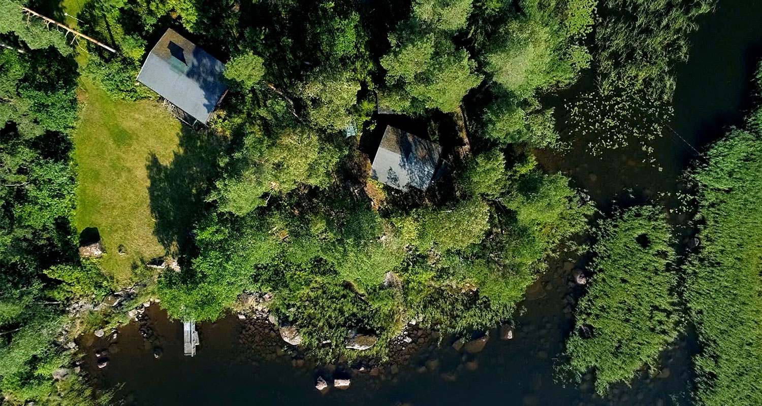 Ilmakuva kahdesta pikkutuvasta metsäisellä niemellä, laituri järven tummien vesien äärellä