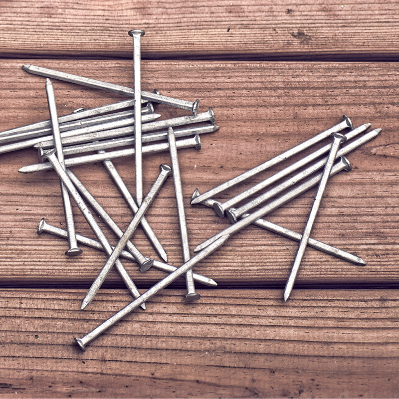 Hopeanvärisiä nauloja satunnaisesti levällään ruskealla lankkupöydällä.