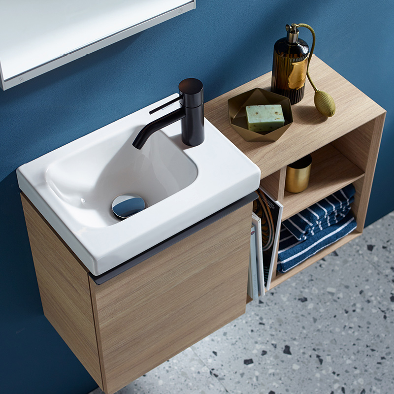 Vaalea tammiviilukaappi seinällä, valkoinen pesuallas, musta hana, sininen seinä ja terrazzo-lattia.