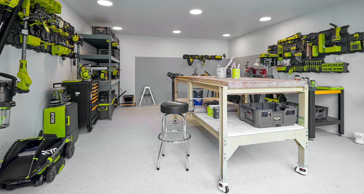 Työpaja, seinillä ja hyllyssä vihreä-mustia Ryobi-työkaluja, keskellä puinen työtaso ja jakkara
