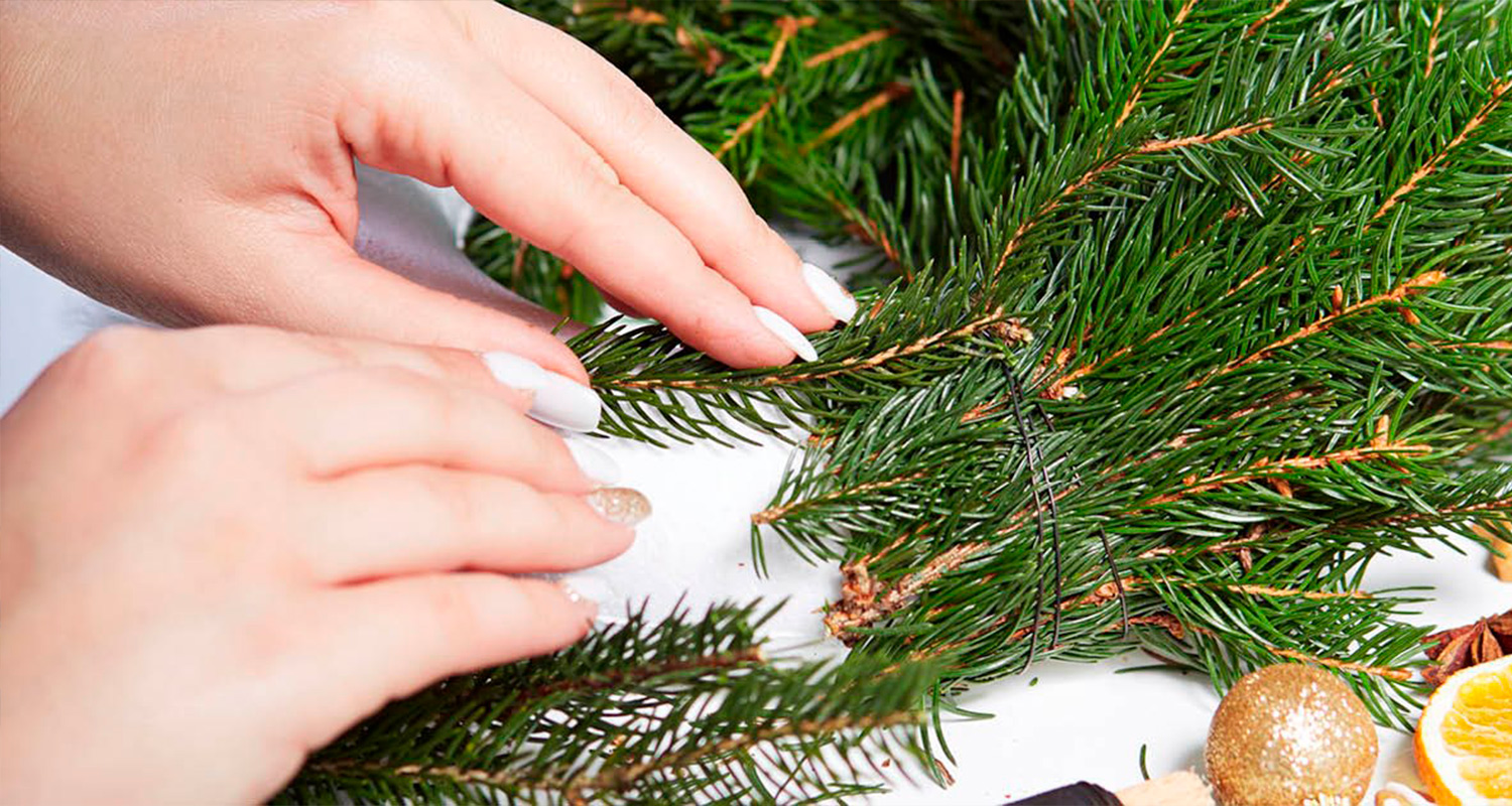 Nainen rakentaa joulukranssia K-Raudan ohjeilla. Kuvassa joulukranssi, joulukoristeita sekä tarvikkeita.