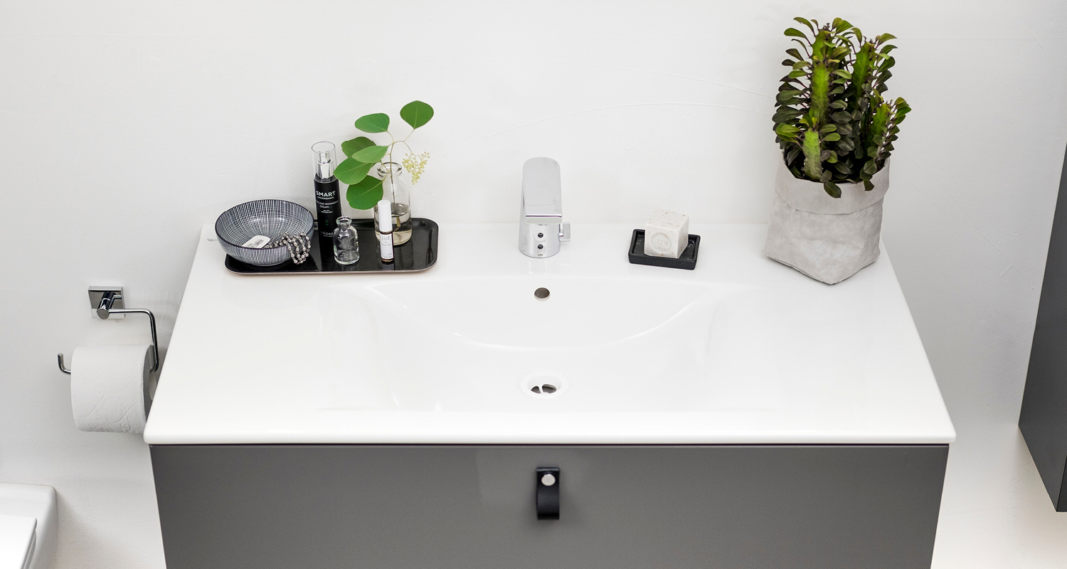 Kylpyhuoneen valkoinen pesuallas harmaa kaappi, musta tarjotin kosmetiikalla ja vihreä kasvi