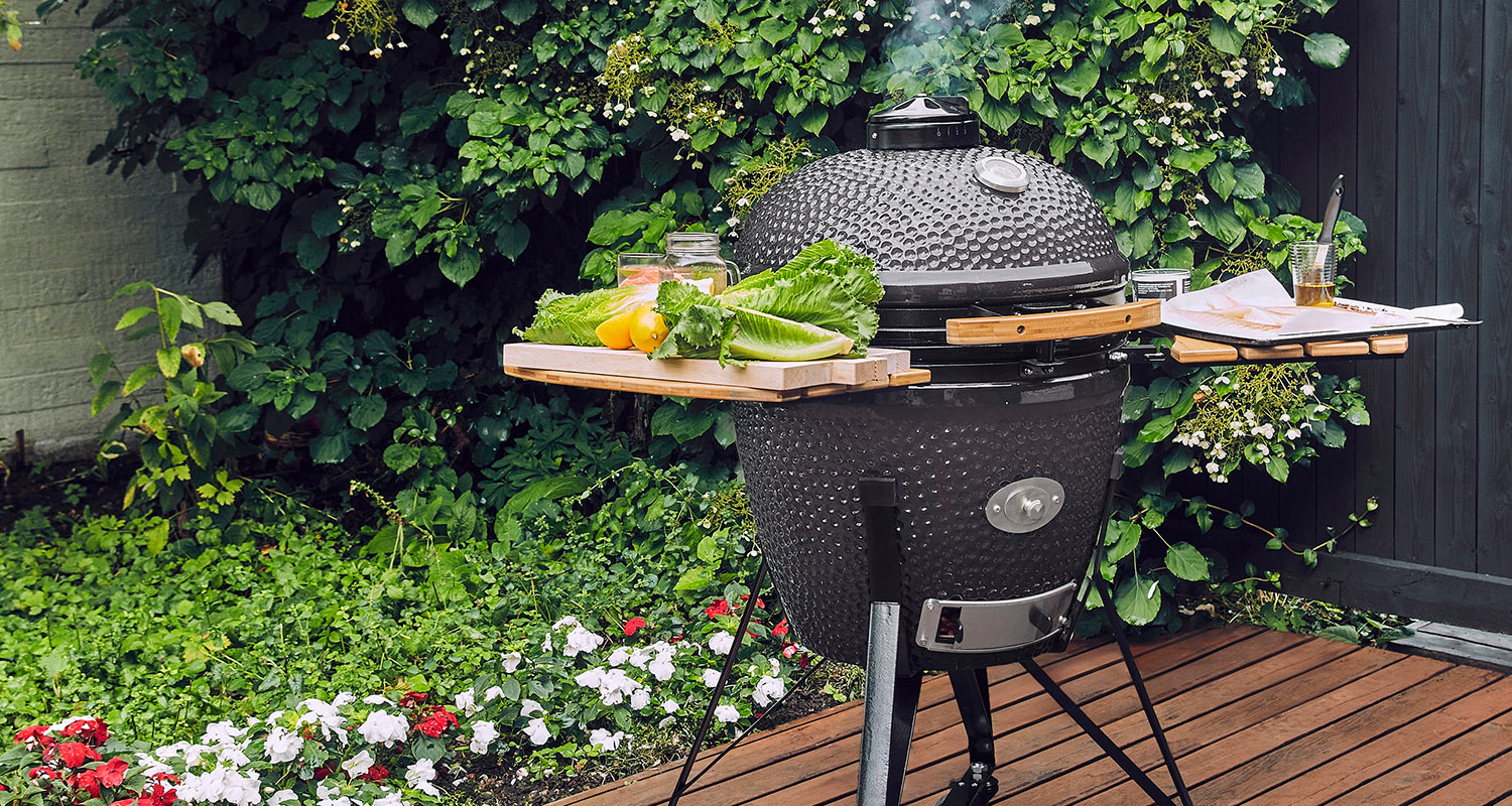 Musta kamado-grilli puisilla tasoilla, salaattia ja sitruunoita, vihreä puutarha ja kukkia.