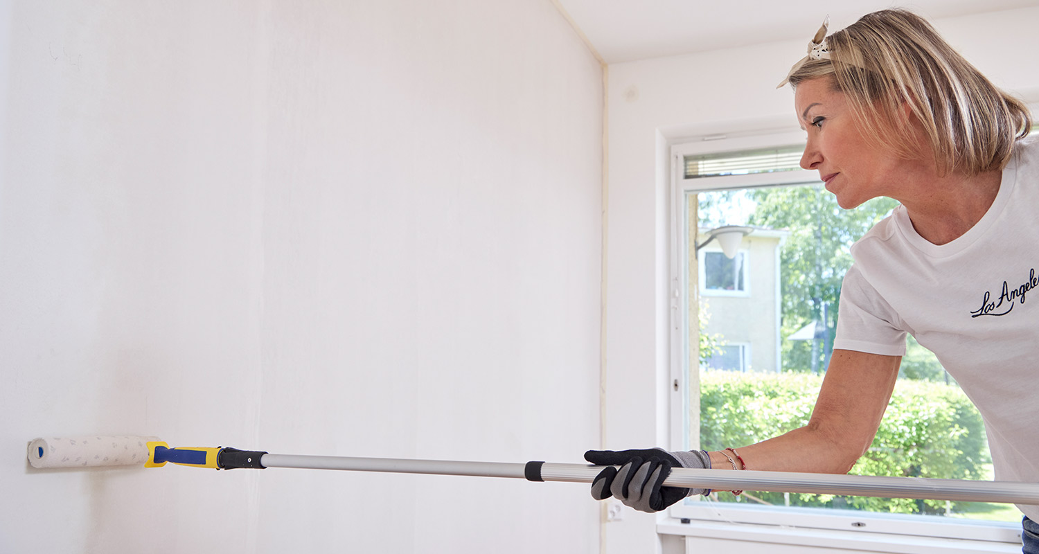 Nainen maalaa sisäseinää vaaleaksi telalla, jossa on jatkovarsi