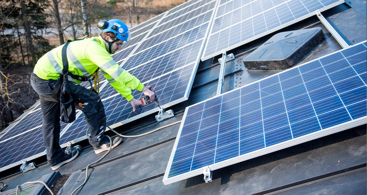 K-Aurinkovoimala ja mies asentamassa aurinkopaneeleita katolle.