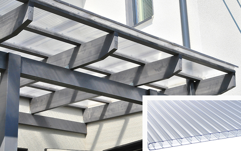 Harmaan puisen pergolakatoksen läpinäkyvä polykarbonaattikatto valkoisen talon edessä