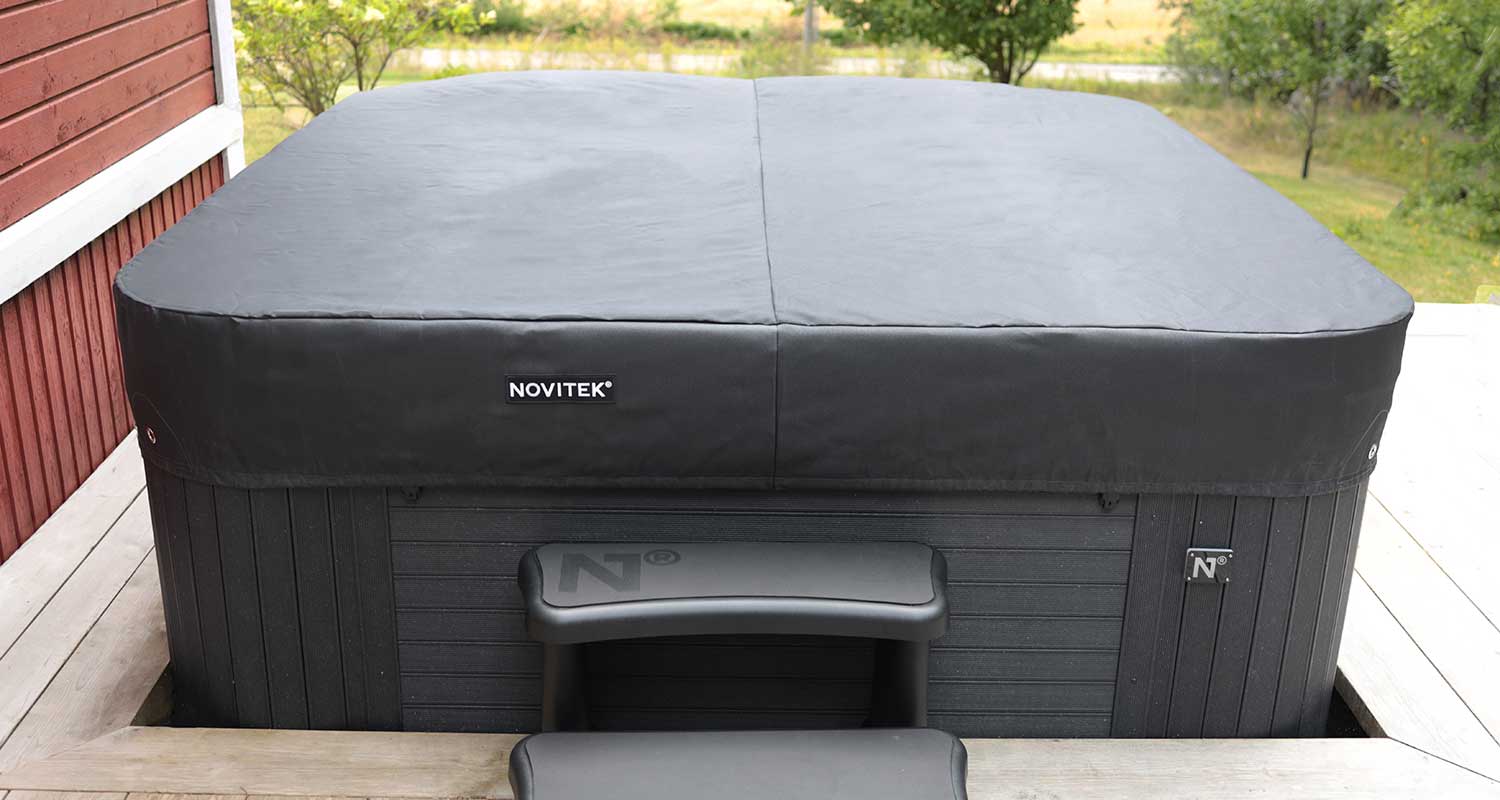 Terassilla musta Novitek-poreallas suojakannella, edessä muoviset portaat ja vihreä puusto taustalla.