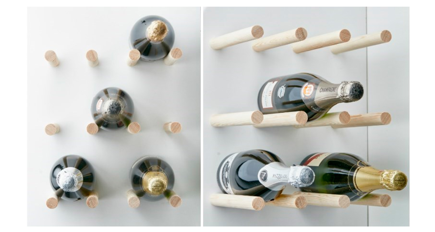 Valkoisella seinällä vaaleat puiset tapit kannattelevat tummia samppanja- ja viinipulloja