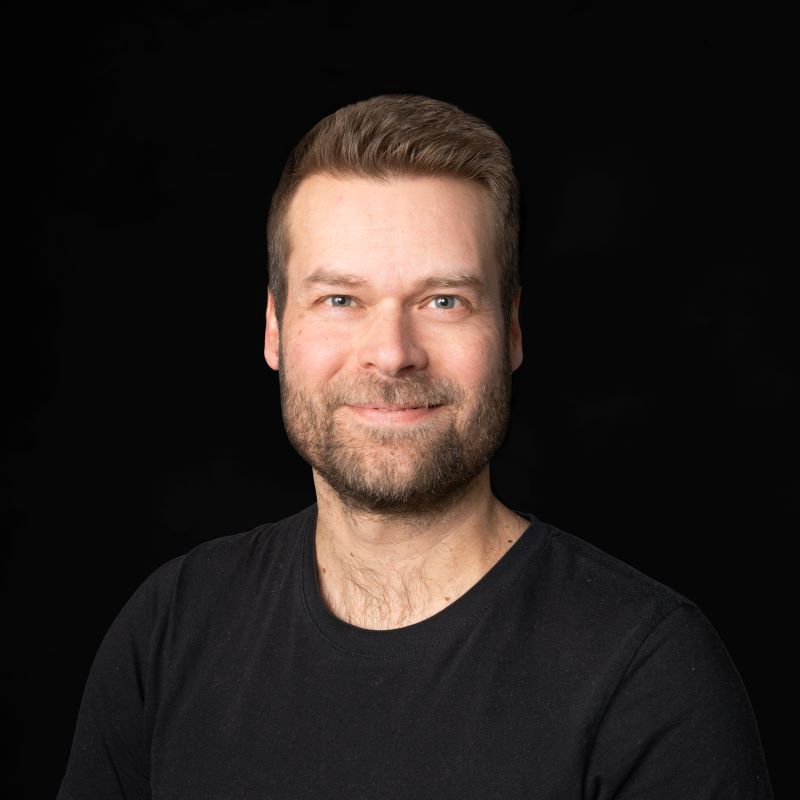 Valossa ruskeahiuksinen mies mustassa t-paidassa tummalla taustalla