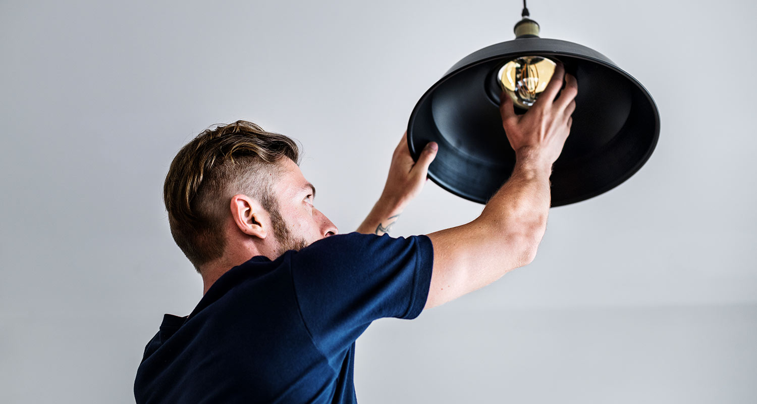 Mies vaihtaa hehkulamppua riippuvalaisimeen.