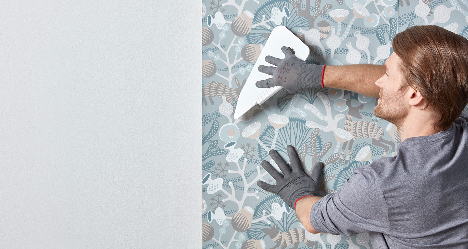 Mies tapetoi seinää K-Raudan sinertävällä kuviotapetilla
