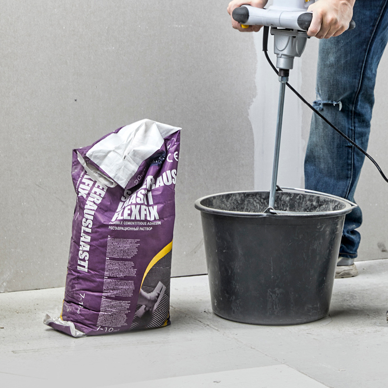 Violetti sementtilaastipussi ja harmaan laastin sekoitus sähkövatkaimella mustassa ämpärissä.