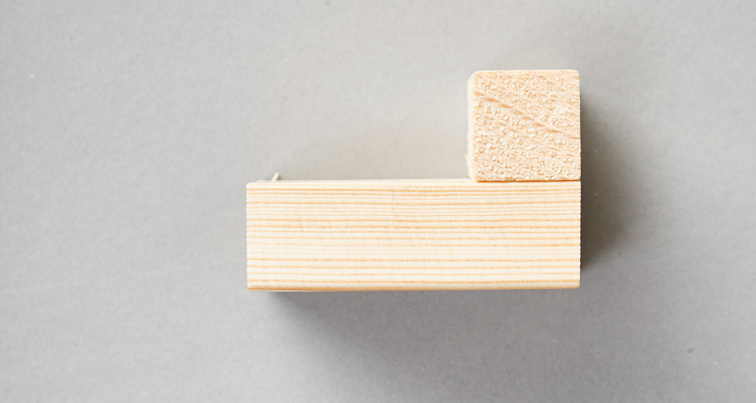 Kaksi vaaleaa puupalikkaa L-muodossa harmaalla taustalla.