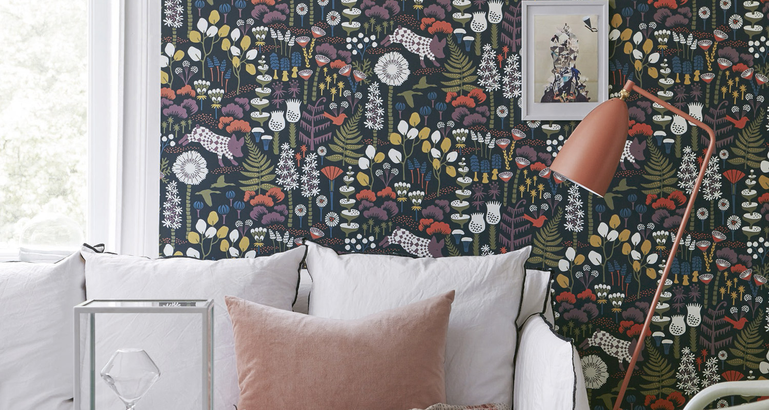 Valkoinen sohva vaaleanpunaisella tyynyllä tummansinistä kukkakuosia vasten ja korallin lattiavalaisin.