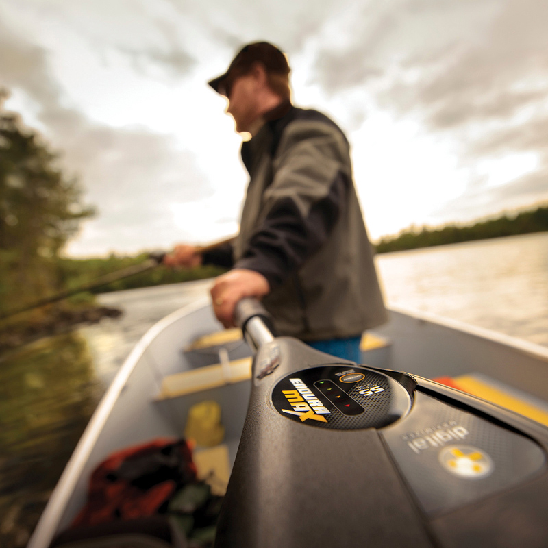 Henkilö kalastaa ja ohjaa sähköperämoottorilla soutuvenettä järvellä, metsää ja pilviä taustalla.