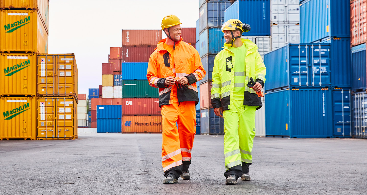 Kaksi työmiestä juttelemassa keskenään Vuosaaren satamassa. Työmiehillä on yllä K-Raudan PROF Workwear -työvaatteet.