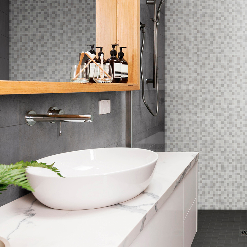 Valkoinen pyöreä allas marmoritasolla, harmaa mosaiikkiseinä, puuhylly saippua- ja hammastelineillä.