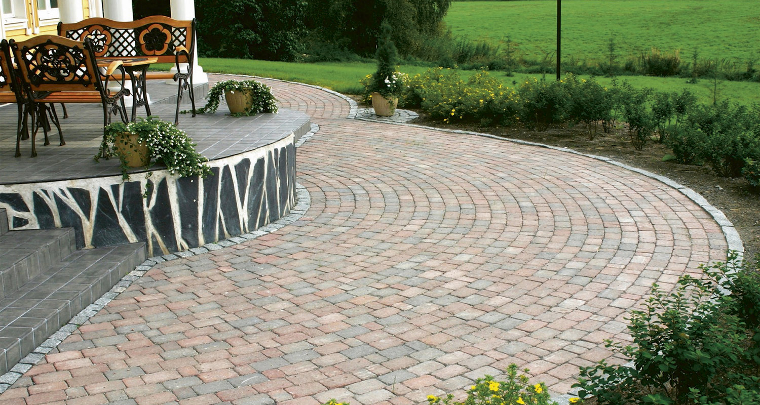 Punertavaharmaa kaareva tiilipatio, korotettu terassi mustavalkoisin kivisivuin, penkkejä ja ruukkuja.