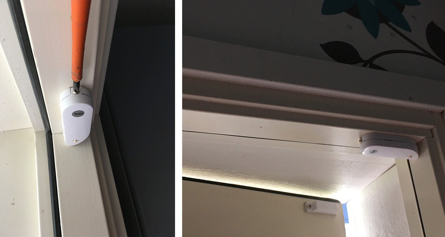 Kaksi pientä valkoista Yale-magneettikoskettimen anturia oven yläkarmeissa, yksi oranssijohdolla.