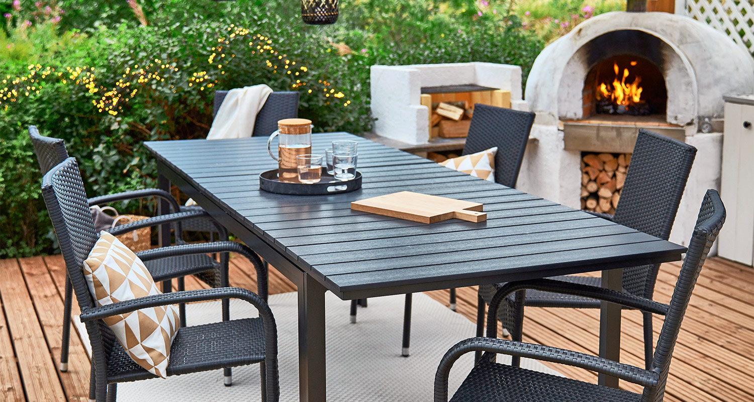 Kaunis ja katettu terassi, jossa on puutarhakalusteet sekä valettu grilli.