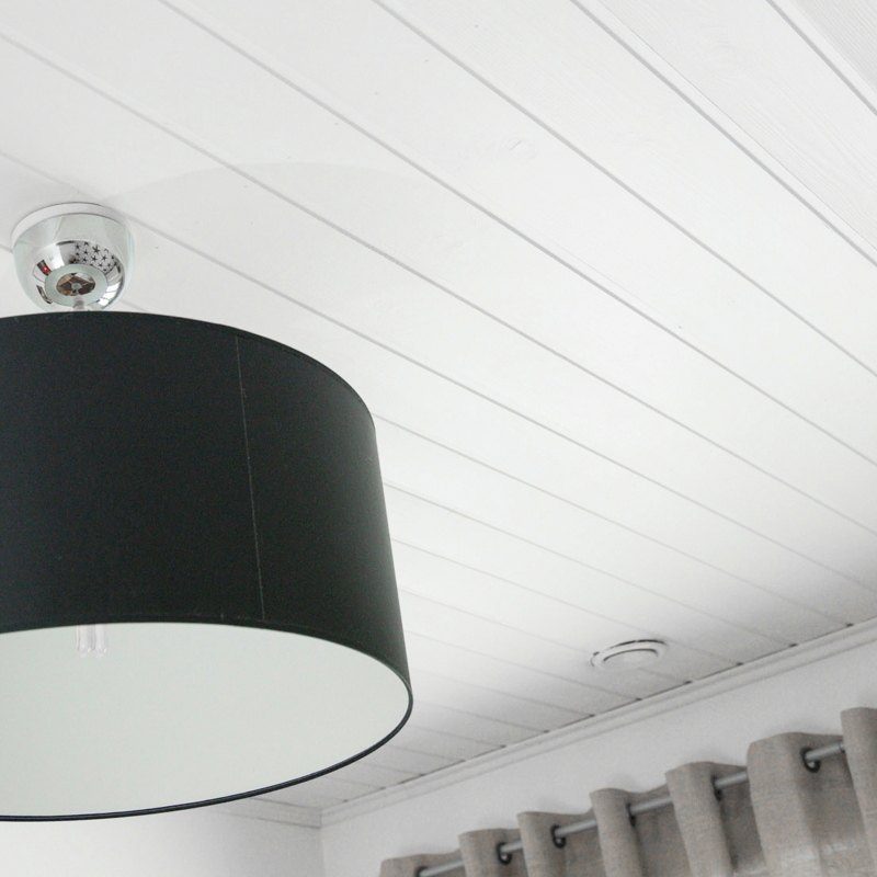 Kuvassa valkoiseksi maalattu paneelikatto ja musta kattovalaisin.