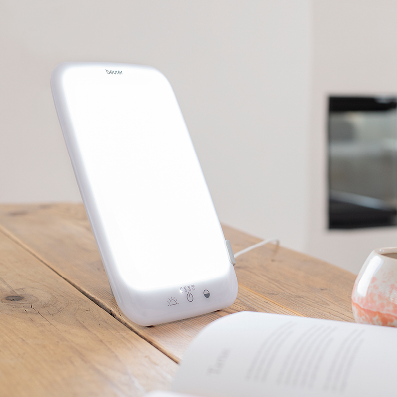 Valkoinen valohoitolamppu puupöydällä, kirkas LED-valo, avoin kirja ja muki taustalla