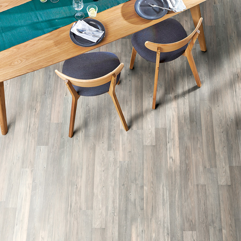 Ylhäältä: vaalea puupöytä turkoosilla kaitaliinalla, lautaset ja kaksi harmaansinistä tuolia