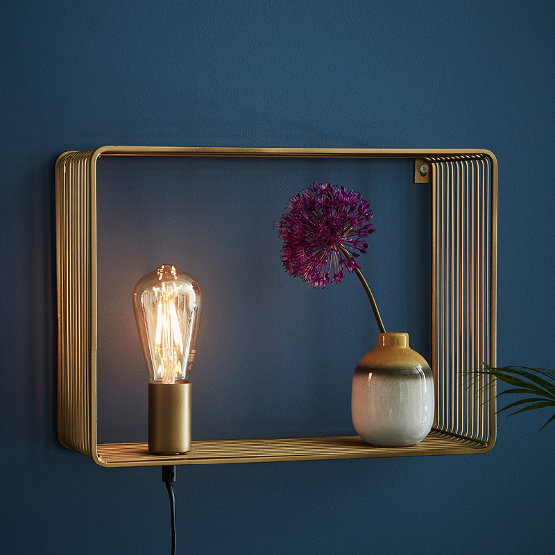 Kultainen avohylly tummansinistä seinää vasten, Edison-lamppu ja maljakossa violetti kukka.